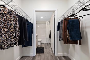 a walk in closet with clothes hanging on a rack and a bathroom with a toilet